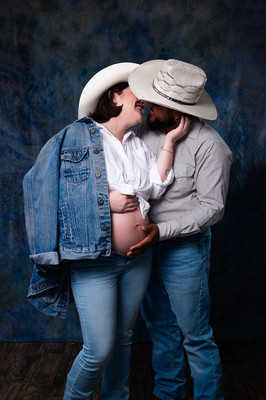  Pareja en espera de su bebé posando en estudio con fondo azul y atuendo vaquero