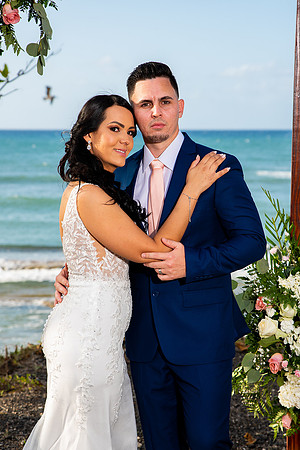 "Pareja de novios caminando en la orilla de la playa al atardecer."