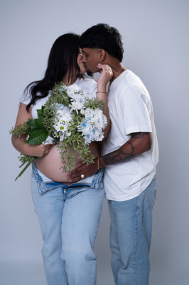 Fotografía de pareja embarazada abrazados con blusas blancas y jeans en estudio de maternidad en Aguadilla, PR