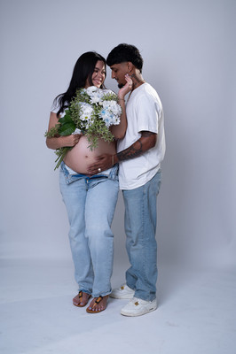Fotografía de pareja embarazada abrazados con blusas blancas y jeans en estudio de maternidad en Aguadilla, PR