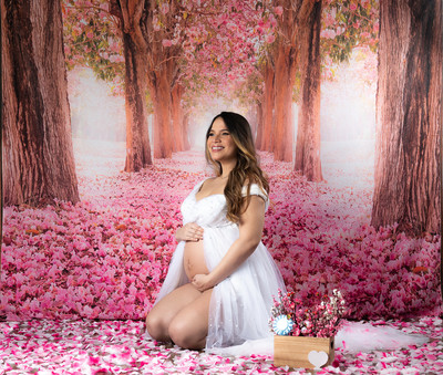 Mujer embarazada en un estudio fotográfico con decoración de flores rosadas.