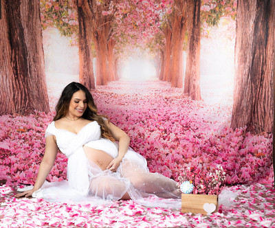 Mujer embarazada en un estudio fotográfico con decoración de flores rosadas.