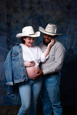 Pareja en espera de su bebé posando en estudio con fondo azul y atuendo vaquero