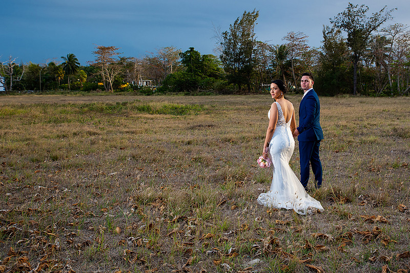 "Pareja de novios caminando en la orilla de la playa al atardecer."