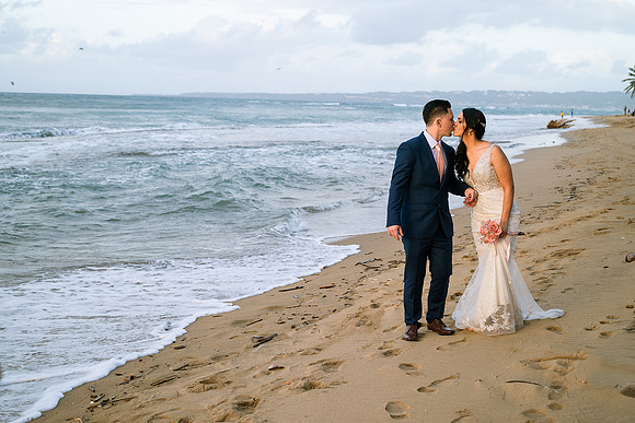 "Pareja de novios caminando en la orilla de la playa al atardecer."